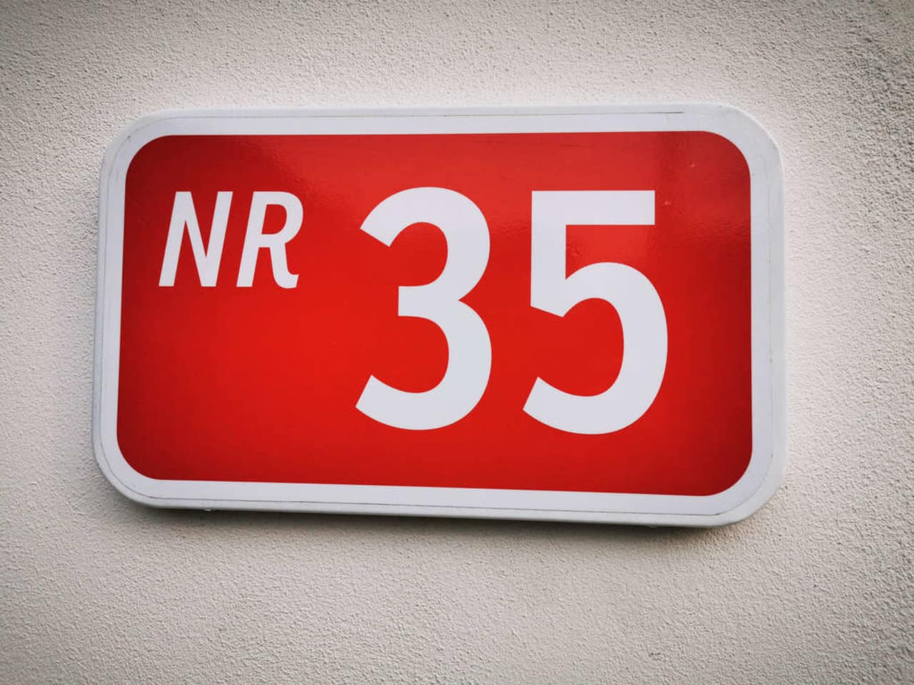 Ilustrando treinamento nr 35, uma placa vermelha escrito "nr 35" numa parede branca