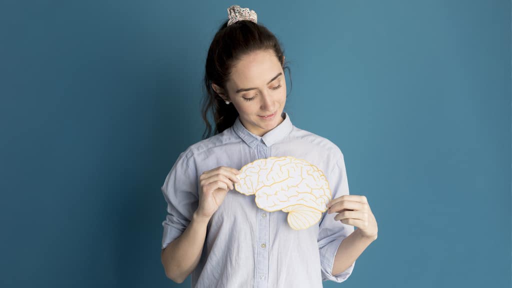 Mulher com sorriso sutil segurando um desenho de cérebro próximo a altura do coração, simbolizando os benefícios da ergonomia cognitiva