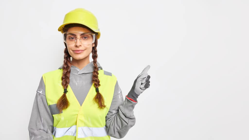 Uma profissional com EPIs como coleta, capacete, óculos de proteção e luvas apontando para cima, simbolizando o Laudo técnico de condições ambientais do trabalho