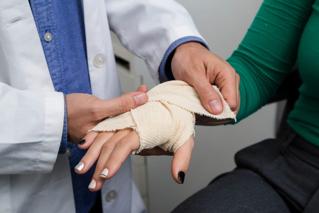 Médico enfaixando a mão de uma paciente, simbolizando doenças ocupacionais