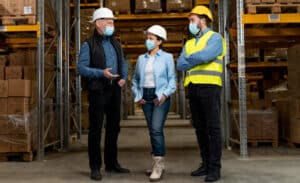 Três profissionais usando EPIs como capacetes, máscaras e colete, simbolizando a nova NR-5